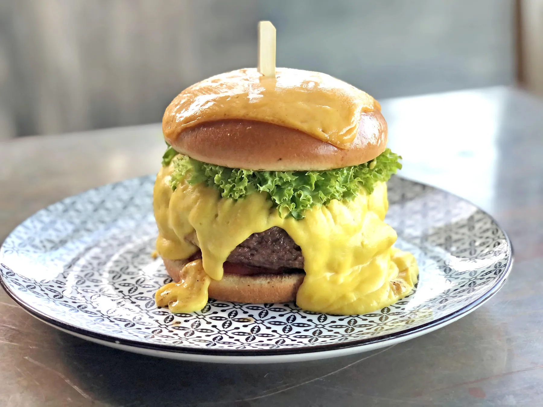 Cheeseburger covered with melted cheese on a patterned plate