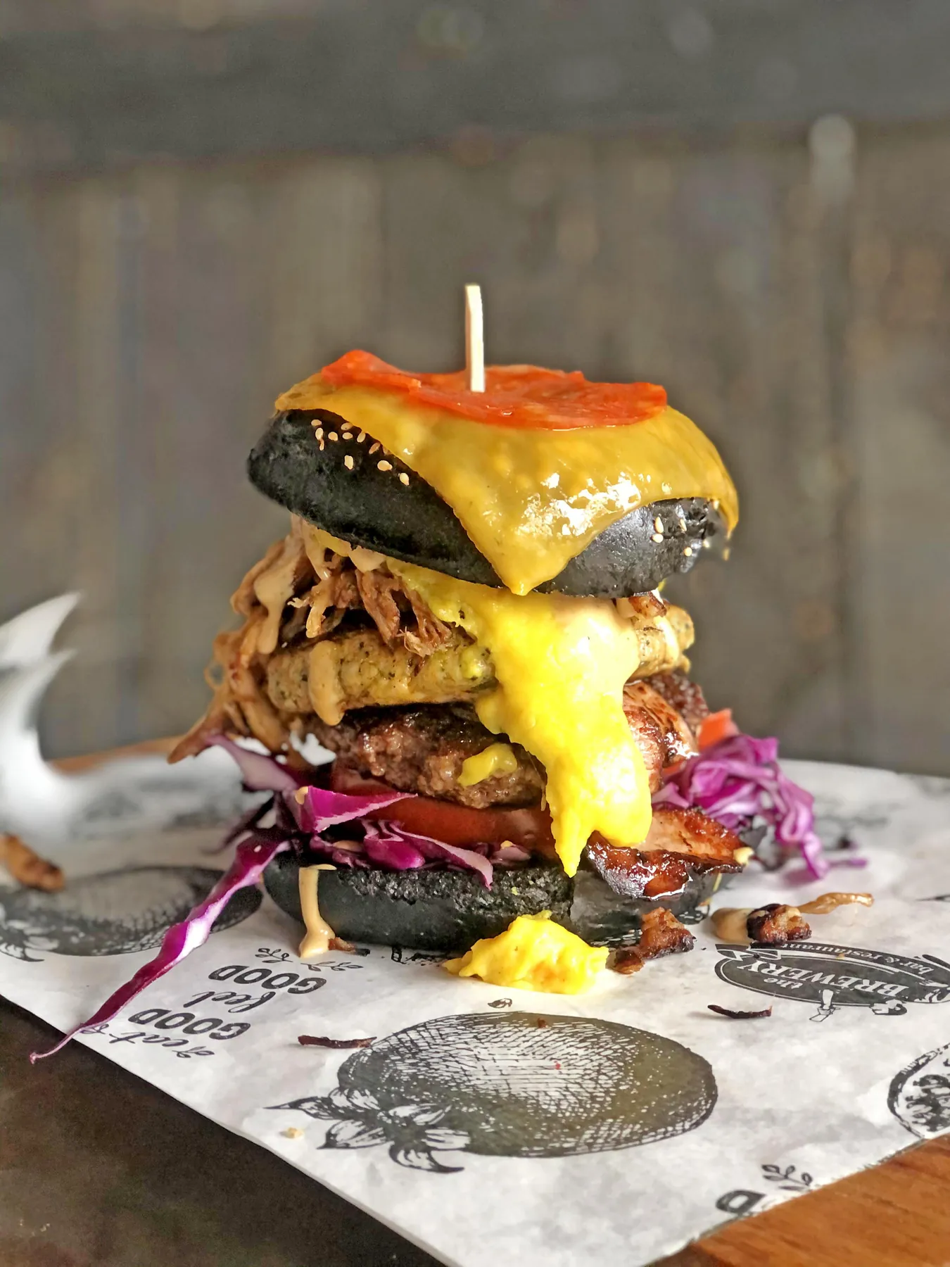 A tall loaded burger in a black sesame bun with melted cheese